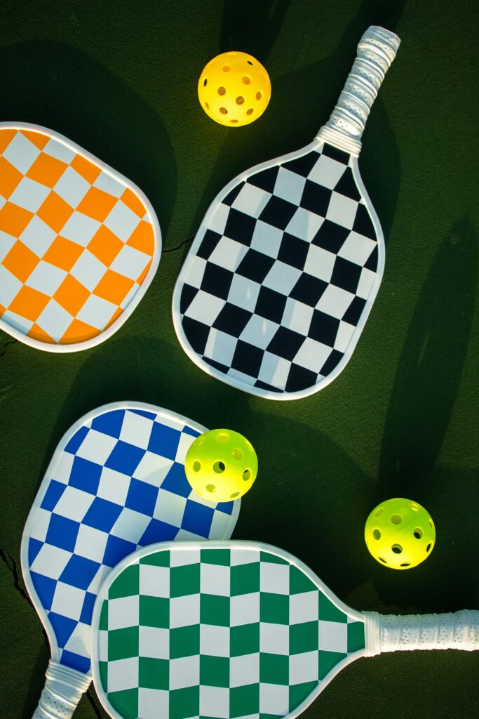 Vibrant checkered paddles and balls create a lively sports theme on green court background.
